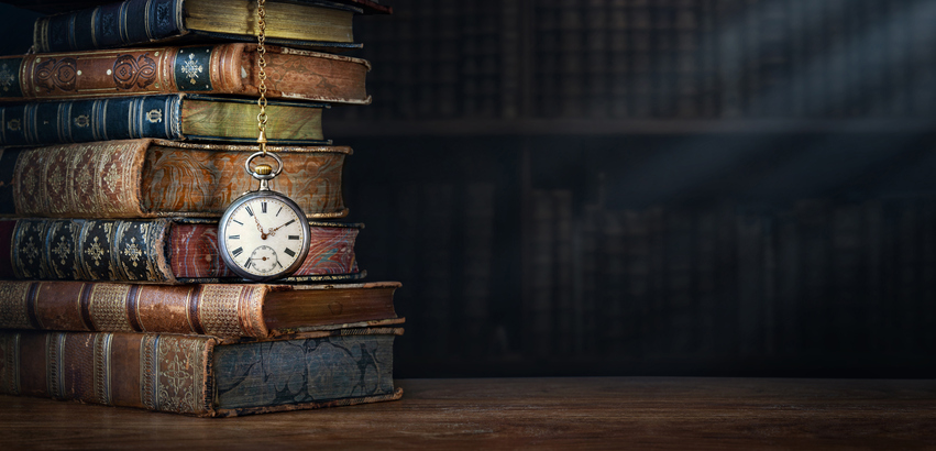 A stack of old books with a pocket watch hanging on them