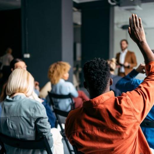 People sitting in a conference room and raising hands to ask questions