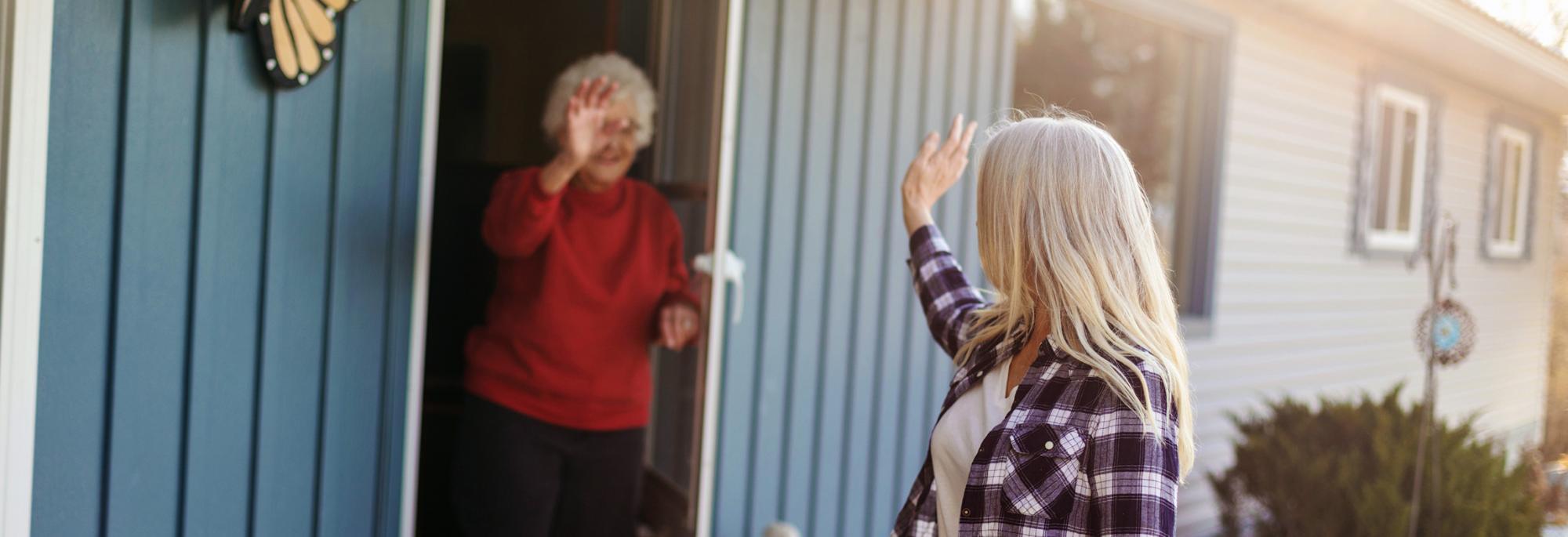 Volunteer waving to a senior citizen after dropping off food