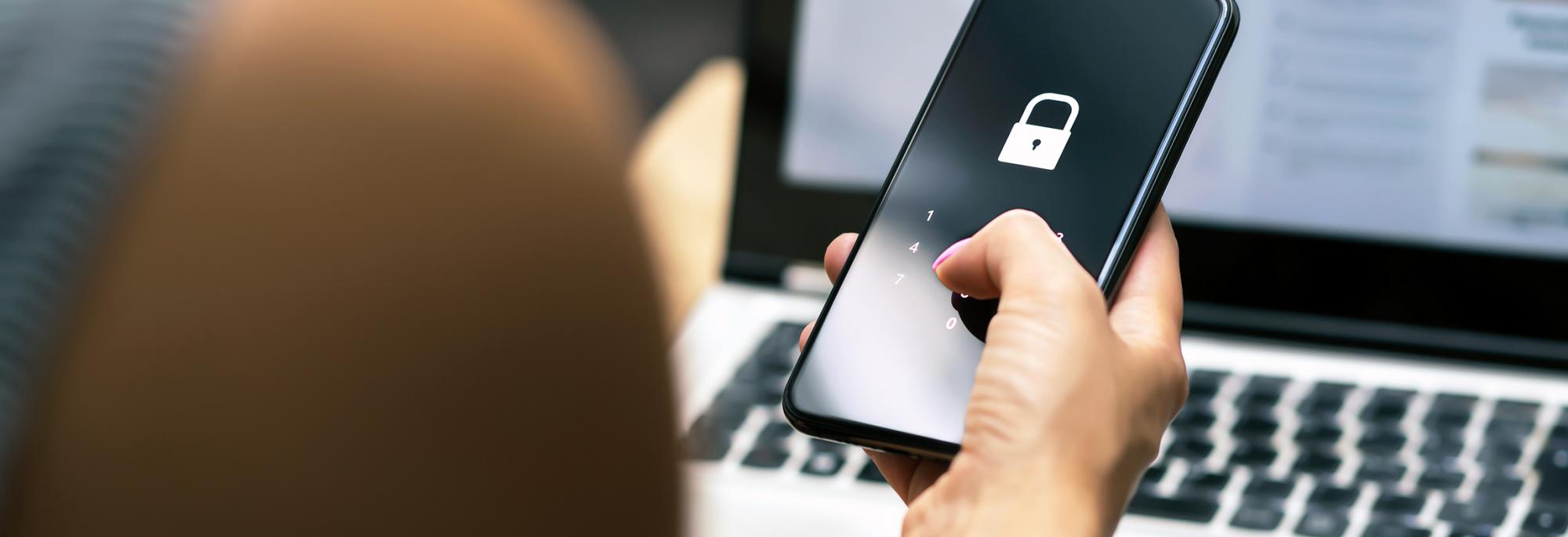 Person holding a cell phone in front of a laptop