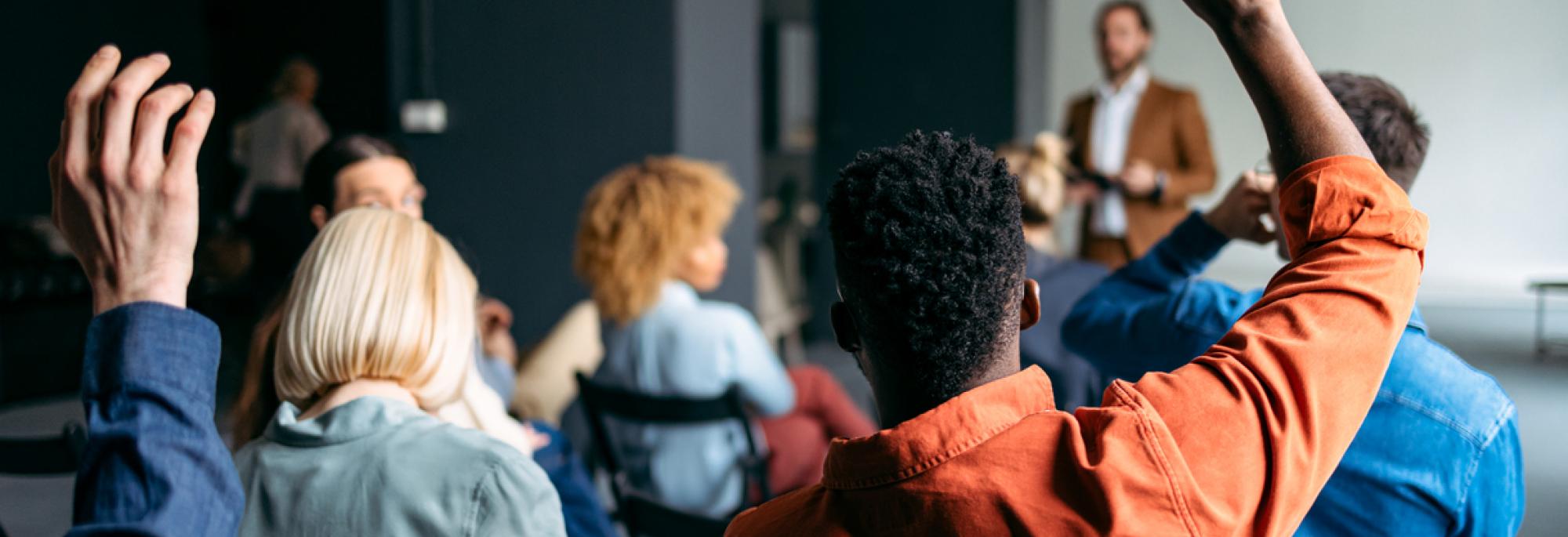 People sitting in a conference room and raising hands to ask questions