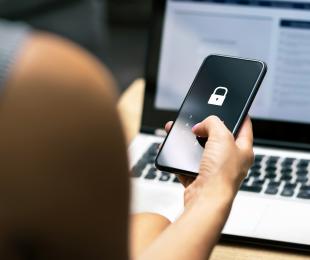 Person holding a cell phone in front of a laptop