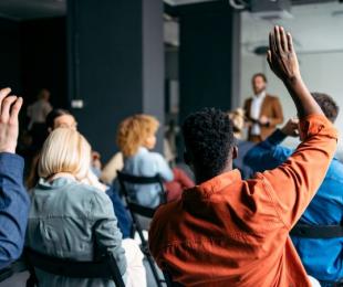 People sitting in a conference room and raising hands to ask questions