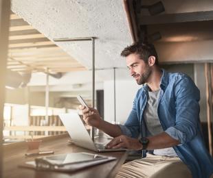 Man working on laptop and looking at mobile phone